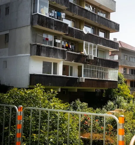 Curtea unui bloc cu balcoane închise, rufe puse la uscat și tufe verzi în față